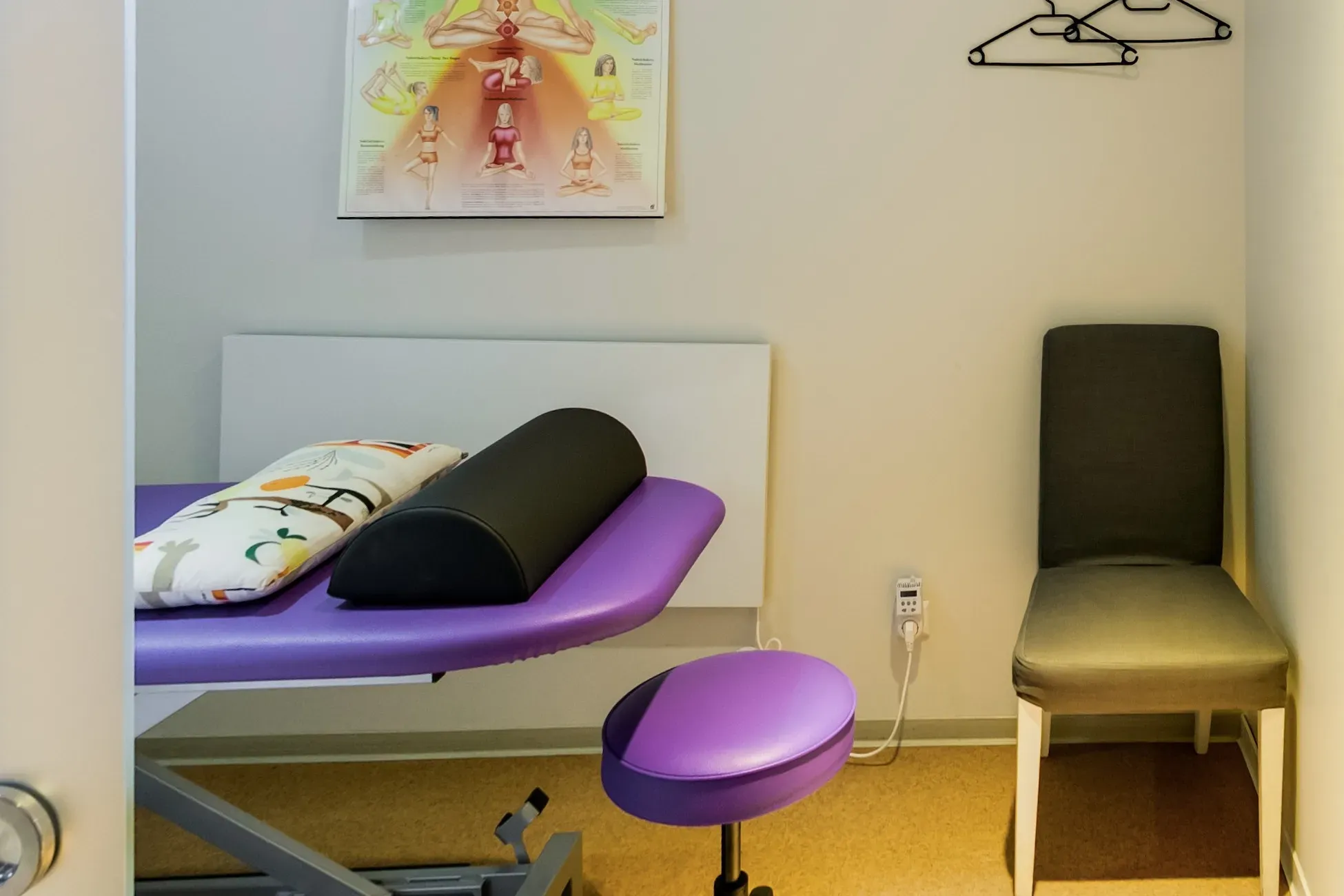 Behandlungsraum mit violetter Therapieliege, Lagerungsrolle, Hocker und Stuhl